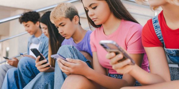Group of serious multiracial teenagers holding mobile phones, watching video, communication online sitting on the street. Technology addiction concept